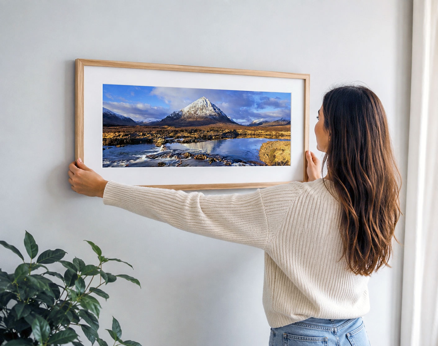 An oak-framed print of Buachaille Etive Mòr being hung on a plain wall